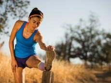 A multiethnic female runner stretches and trains for running on trails in the hilly countryside at sunset.